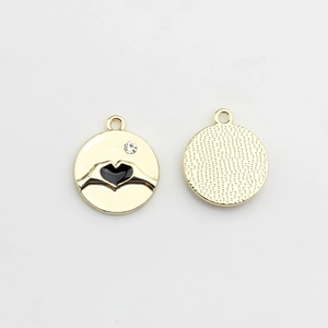 Detail view of round gold pendants with black enamel heart gesture and crystal inlay