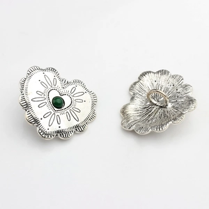Detailed close-up of vintage silver alloy heart button with green stone and scalloped edge