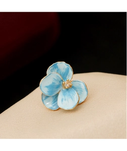 Macro shot of blue enamel flower brooch with gold edges and central zircon detail