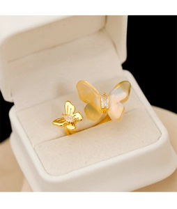 Détail d'une bague papillon dorée aux ailes irisées et pierres dans son écrin blanc