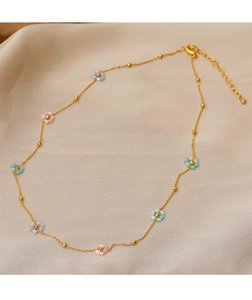 Detail of a gold chain necklace with colorful beaded flowers on soft beige silk fabric