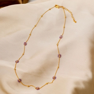 Dainty gold chain necklace with purple beaded flowers on champagne silk background