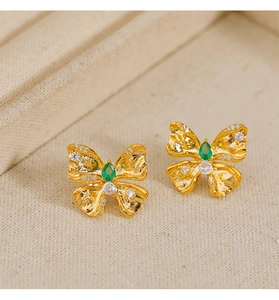 Primer plano de pendientes mariposa dorados con textura martillada y gema verde esmeralda