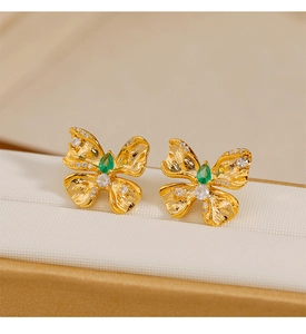Detalle de pendientes de mariposa dorados con piedra verde de pera y micro-pavé brillante