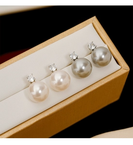 Détail de boucles d'oreilles perles blanches et gris argenté avec zircons sur boîte dorée