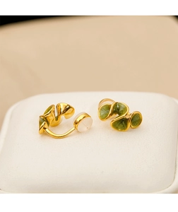 Detail shot of gold cream flower ear clips with green enamel on a soft white display pad