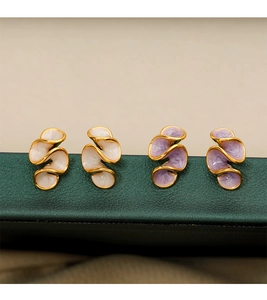 Macro shot of cream and purple enamel S-shaped earrings with gold trim on dark green leather