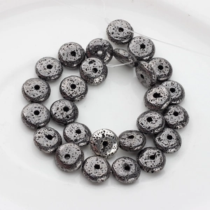 Macro shot of dark grey lava stone beads with natural texture on a white plate