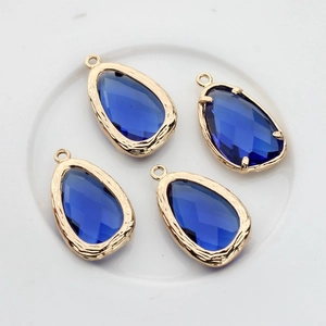 Detailed view of four 14K gold-plated teardrop glass pendants with faceted navy blue stones