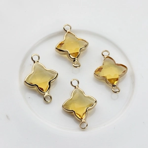 Détail de breloques trèfle en cristal jaune avec bordure dorée et doubles anneaux pour DIY