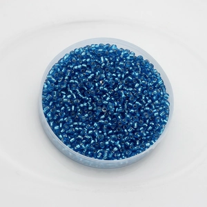 Macro shot of vibrant blue 2mm glass seed beads for DIY jewelry making in a round container