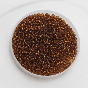 Macro detail of 2mm amber glass seed beads in a round storage box for DIY jewelry