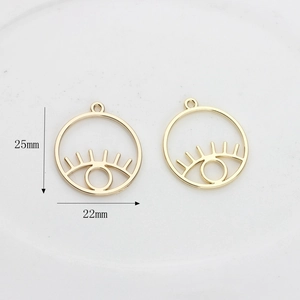 Détail macro de pendentifs yeux évidés dorés avec cils et dimensions précises