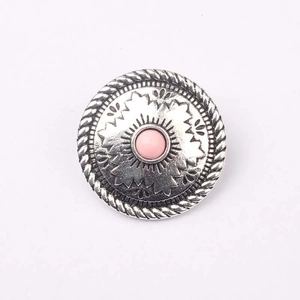 Dettaglio di un concho tondo in argento antico con resina rosa e rilievo floreale