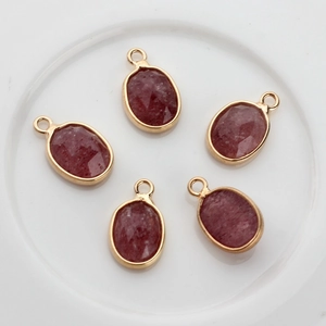 Detalle de cinco colgantes de piedra natural roja facetada con borde ovalado dorado