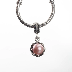 Detalle de un dije de flor plateada con perla rosa en una pulsera de serpiente