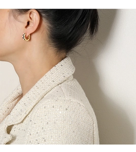 Détail d'une boucle d'oreille créole dorée avec motif en damier noir et blanc sur modèle