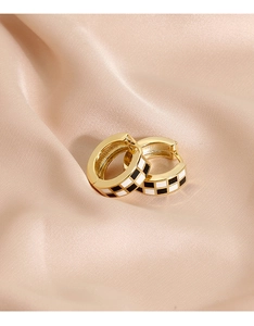 Détail de créoles dorées à damier sur soie champagne montrant la finition émaillée