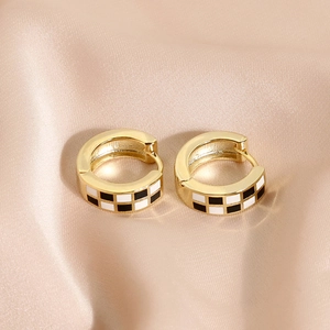Boucles d'oreilles créoles dorées avec émail à damier noir et blanc sur fond satiné