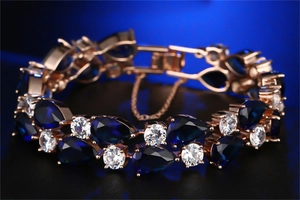 Detail of rose gold bracelet featuring blue pear-shaped stone and safety chain