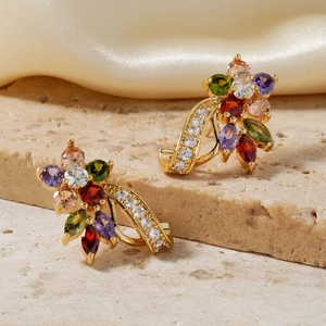 Detail of 18K gold floral earrings set with colorful zircon stones on stone background