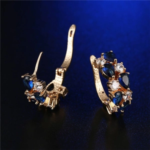 Dettaglio di orecchini dorati con pietre blu a goccia e accenti in zirconi scintillanti