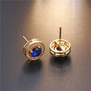 Macro view of gold round stud earrings with blue sapphire-like stone and zircon halo