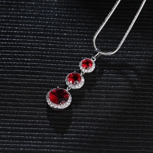 Close-up of triple graduated red ruby pendant with crystal halo on silver chain