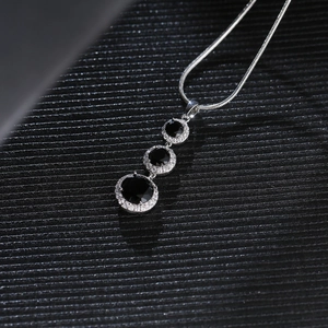 Detail of three black round stones necklace with white crystal halo on a black fabric background