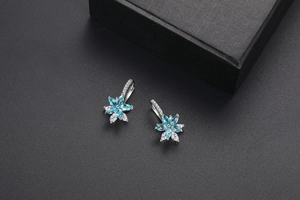Détail de boucles d'oreilles fleurs avec pierres marquises bleu ciel et pavage de zircons