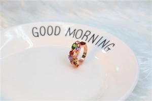 Gros plan d'une bague en or rose sertie de pierres multicolores sur plateau blanc