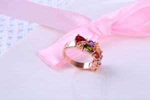 Gros plan d'une bague en or rose avec cristaux colorés et ruban de soie rose