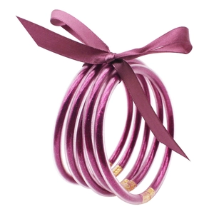 Detalle de cinco pulseras de silicona con purpurina magenta unidas por un lazo de satén