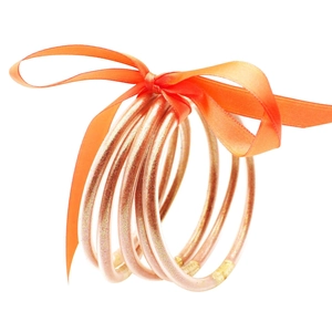 Detalle de pulseras de silicona con purpurina multicapa con un vibrante lazo de seda naranja