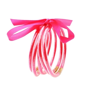 Detalle de cinco pulseras de silicona con purpurina rosa y un lazo de satén decorativo
