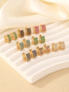 Makro-Detail vergoldeter Huggie-Ohrringe mit farbigem Zirkonia und geometrischen Mustern