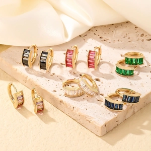 Elegant gold earrings set with colorful rectangular zircons on beige stone background