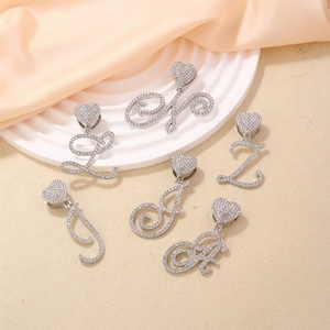 Collane argentate con lettere corsive, chiusura a cuore e strass su piedistallo beige