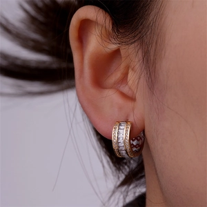 Close-up of gold huggie earrings with baguette and round zircon stones worn by a model