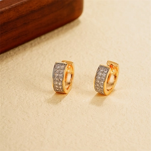 Dettaglio di ampi orecchini a cerchio in oro 18k con zirconi pavé su fondo beige