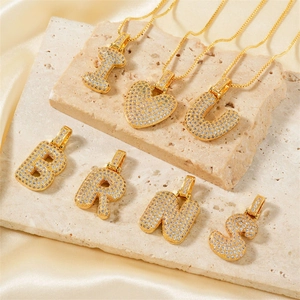 Detailed view of gold plated alphabet pendants with pavé zircon stones on silk fabric