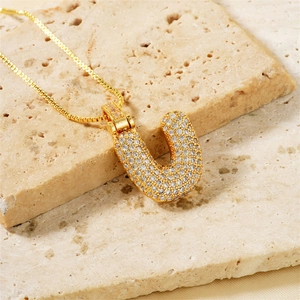 Macro shot of gold tone letter U pendant with cubic zirconia on a box chain necklace