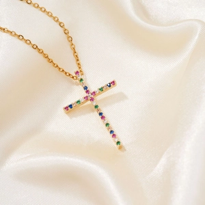 Detalle del colgante de cruz con gemas de colores sobre fondo de raso champán