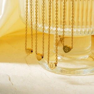 Detail of multiple gold-tone heart pendants with engraved letters on delicate O-chains