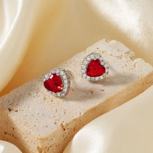 Macro detail of red heart zircon earrings with white halo stones on silk fabric