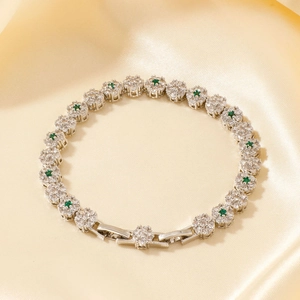 Elegante pulsera floral con circonitas verdes y blancas sobre fondo de seda amarilla