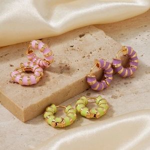 Three pairs of vintage gold hoop earrings with colorful enamel stripes on a stone display