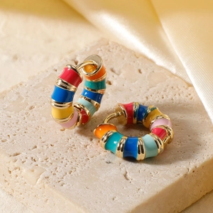 Close-up of rainbow enamel hoop earrings in gold-tone finish on a stone display