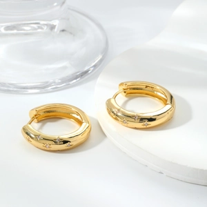 Orecchini a cerchio dorati con stelle incise e zirconi su un supporto bianco elegante