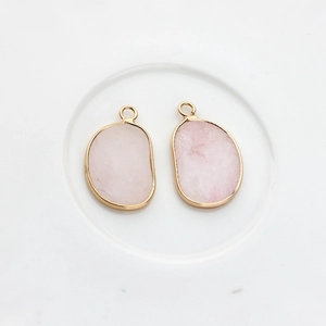 Detail of two irregular pink quartz stone pendants with gold-plated metal frames